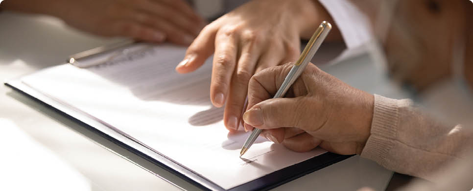 Commercial medicine. Close up of aged woman patient hand signing medical insurance contract at doctor office. Female medic show retired lady client place to put signature on healthcare coverage policy