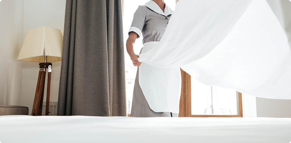 Young hotel maid changing bed sheets