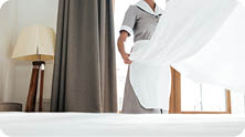 Young hotel maid changing bed sheets